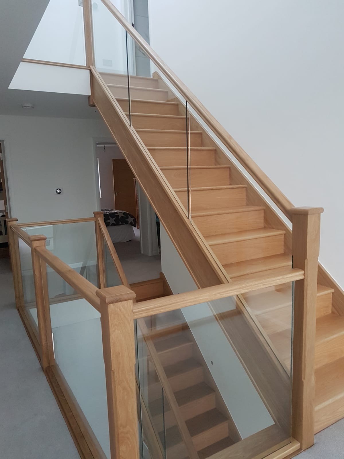 Jasne, drewniane schody z przezroczystymi szklanymi balustradami w nowoczesnym wnętrzu domu, widok z góry na podest.