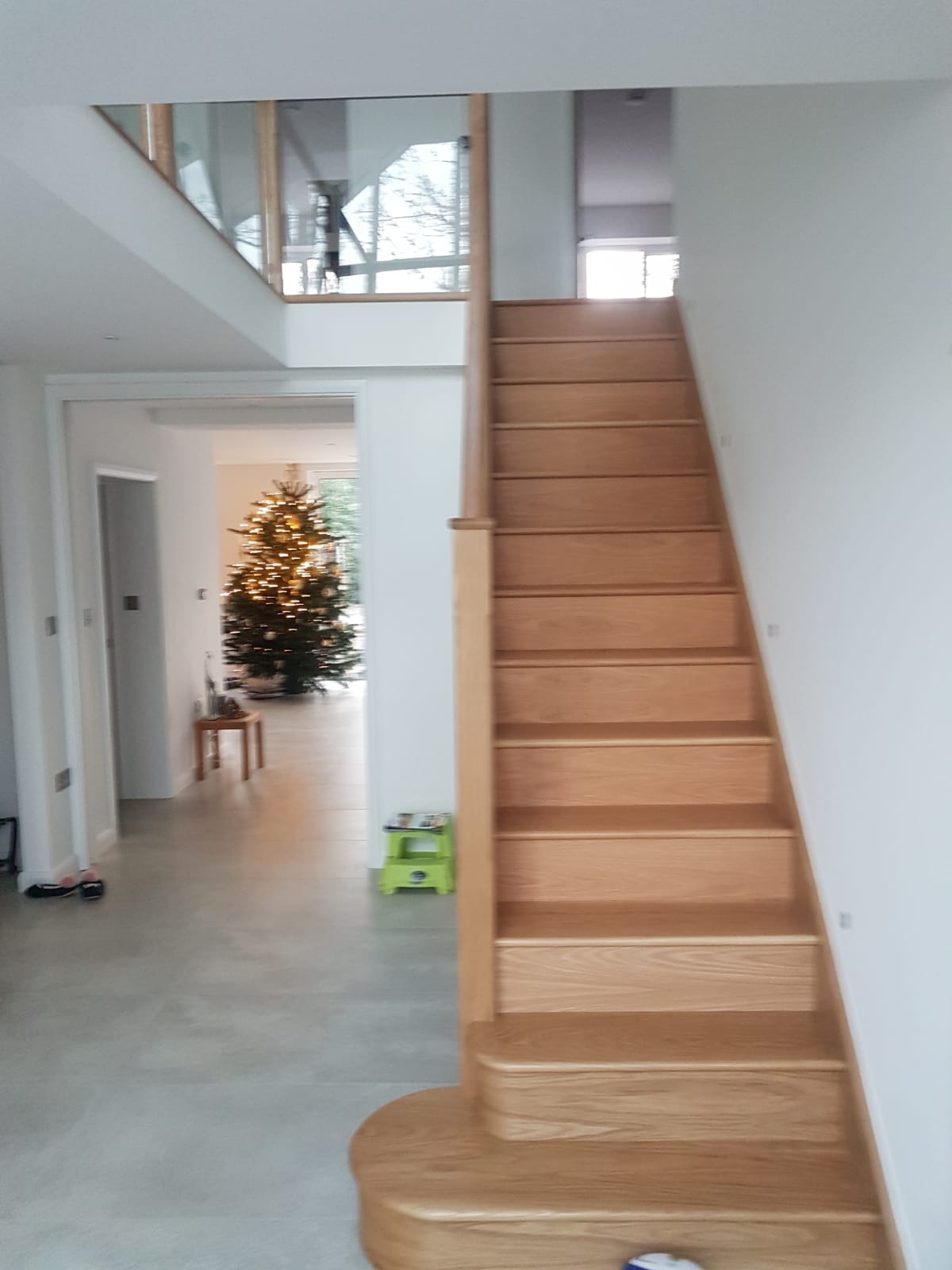 Nowoczesne, drewniane schody w jasnym wnętrzu domu, widok na salon z choinką przez otwarte przejście.