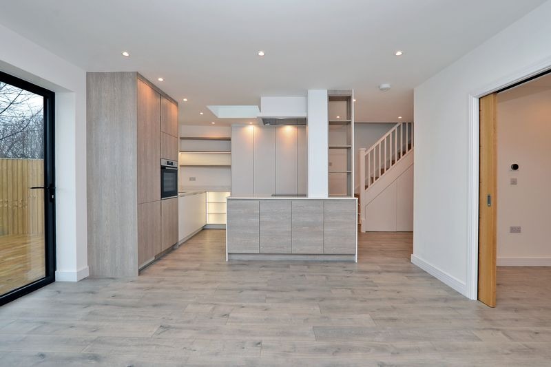 Jasne, nowocześnie urządzone wnętrze z otwartą kuchnią, drewnianą podłogą i schodami; widoczny fragment ogrodu za oknem.