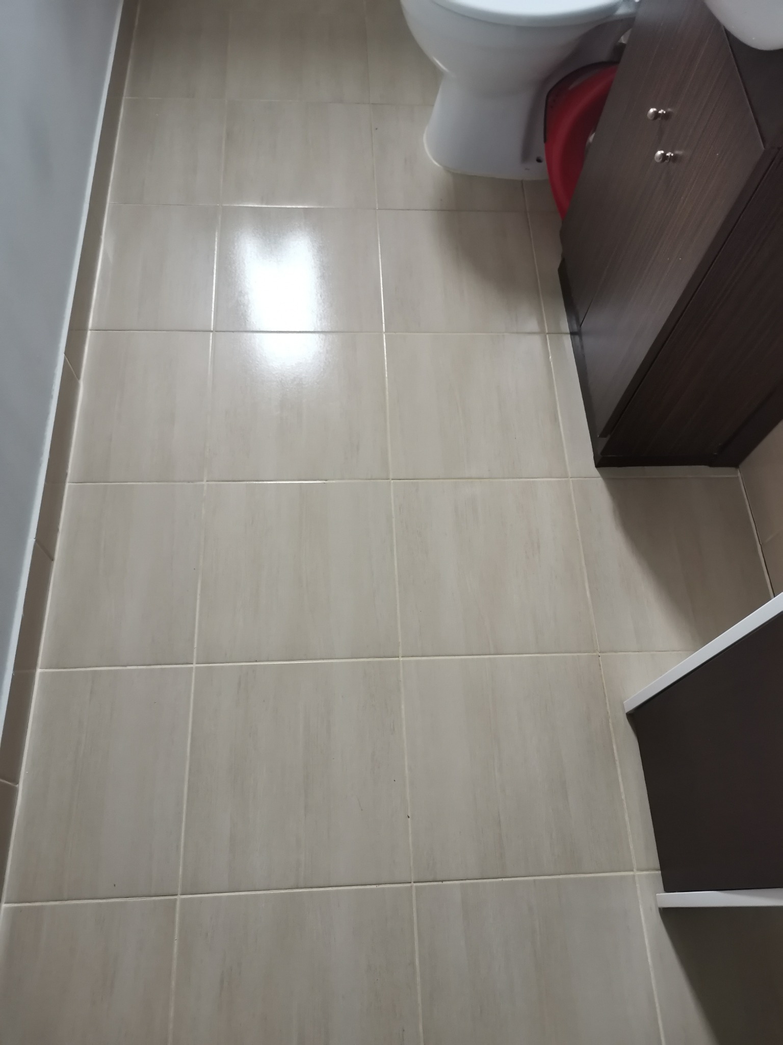 Błyszcząca, beżowa podłoga z płytek w łazience w Grudziądzu, widoczny fragment toalety i szafki pod umywalką.