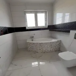 Nowoczesna łazienka z biało-czarną glazurą, marmurową podłogą i obudową wanny z mozaiki, widok na okno z białymi ramami.