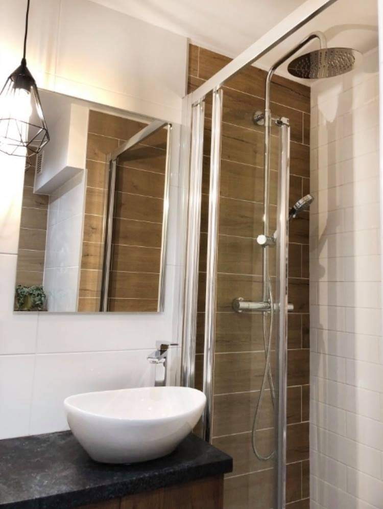 Nowoczesna łazienka z kabiną prysznicową typu walk-in z deszczownicą, umywalką nablatową w kształcie łezki i lustrem z oświetleniem punktowym.