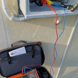 Podłączenie miernika marki Sonel do skrzynki elektrycznej w Rykach, widoczne przewody pomiarowe w kolorach: czerwonym, niebieskim i żółtym oraz otwarty futerał z kablem i instrukcją obsługi.