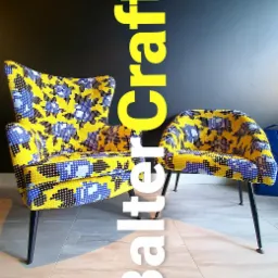 Dwa fotele w stylu retro z żółto-niebieską tapicerką w geometryczne wzory, na czarnych metalowych nóżkach, wykonane na zamówienie w Warszawie. Większy fotel z wysokim oparciem stoi obok mniejszego.