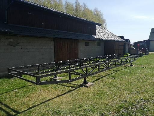 Metalowa konstrukcja szkieletowa na betonowych podstawach, przygotowana pod budowę domu na tle wiejskich zabudowań i traktora.