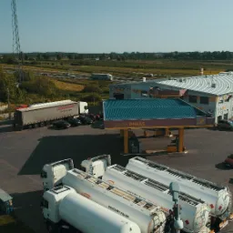 Widok z góry na stację paliw Grupa Pegas z zaparkowanymi cysternami i ciężarówkami, widoczny budynek stacji, dystrybutory i otaczający krajobraz z polami i drogą