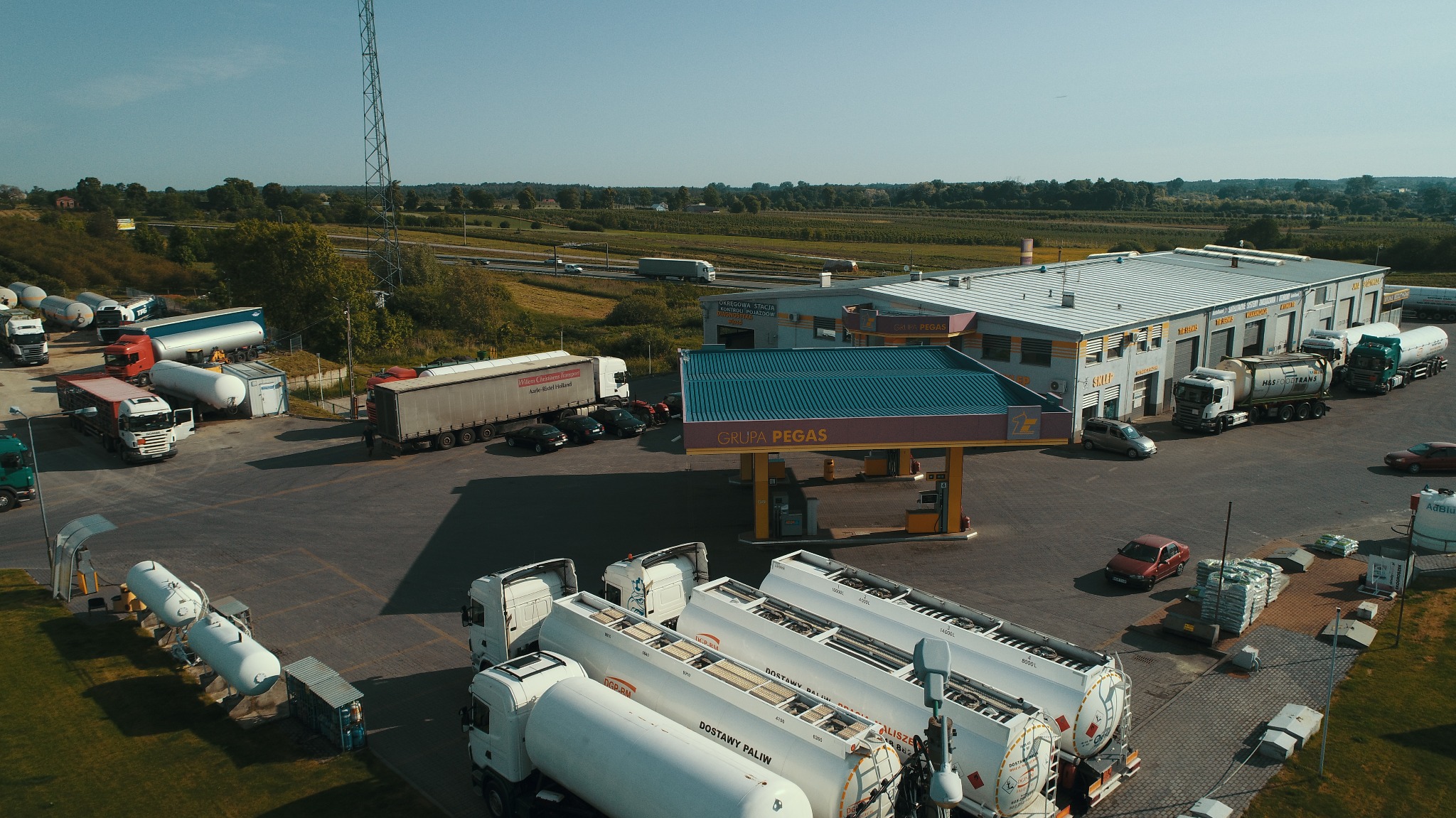 Widok z góry na stację paliw Grupa Pegas z zaparkowanymi cysternami i ciężarówkami, widoczny budynek stacji, dystrybutory i otaczający krajobraz z polami i drogą