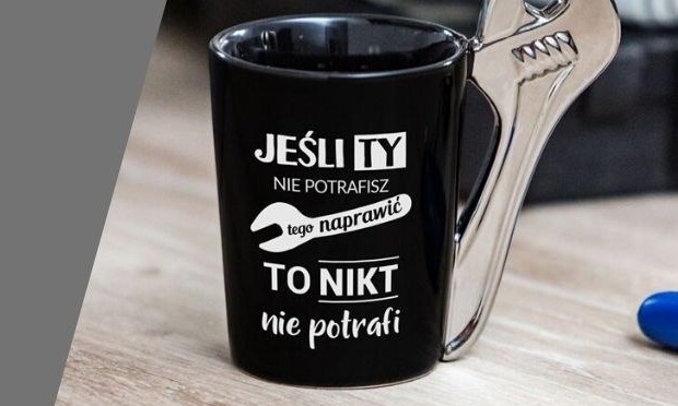 Czarny kubek z białym napisem 'Jeśli Ty nie potrafisz tego naprawić TO NIKT nie potrafi' i rysunkiem klucza francuskiego, z uchwytem w kształcie klucza nastawnego.