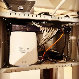 Szafa rack z routerem Orbi, switchem Netgear i anteną Starlink, okablowanie sieciowe wewnątrz szafy.