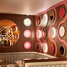 Igor Jasiński Electric Solutions - Stylowe oświetlenie dekoracyjne: okrągłe lampy LED w odcieniach różu i bieli na drewnianej ścianie, odbicie w lustrze i kamera przemysłowa w rogu.
