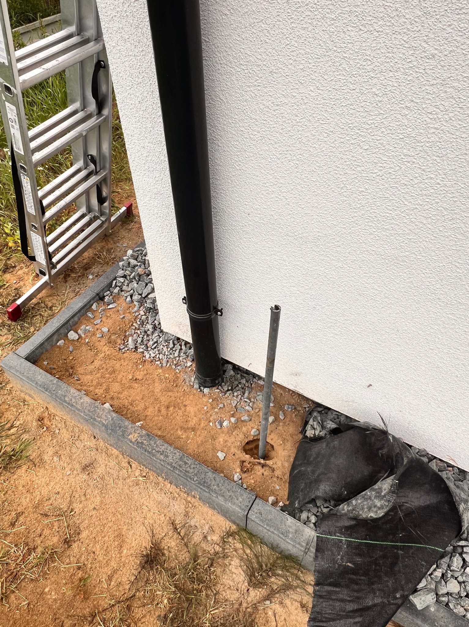 Uziemienie pionowe w trakcie montażu przy ścianie budynku, widoczna rura spustowa i drabina aluminiowa w tle.