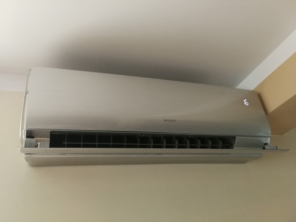 Zamontowany na ścianie klimatyzator marki Gree z wyświetlaczem temperatury, widoczny pod sufitem w jasnym pomieszczeniu.