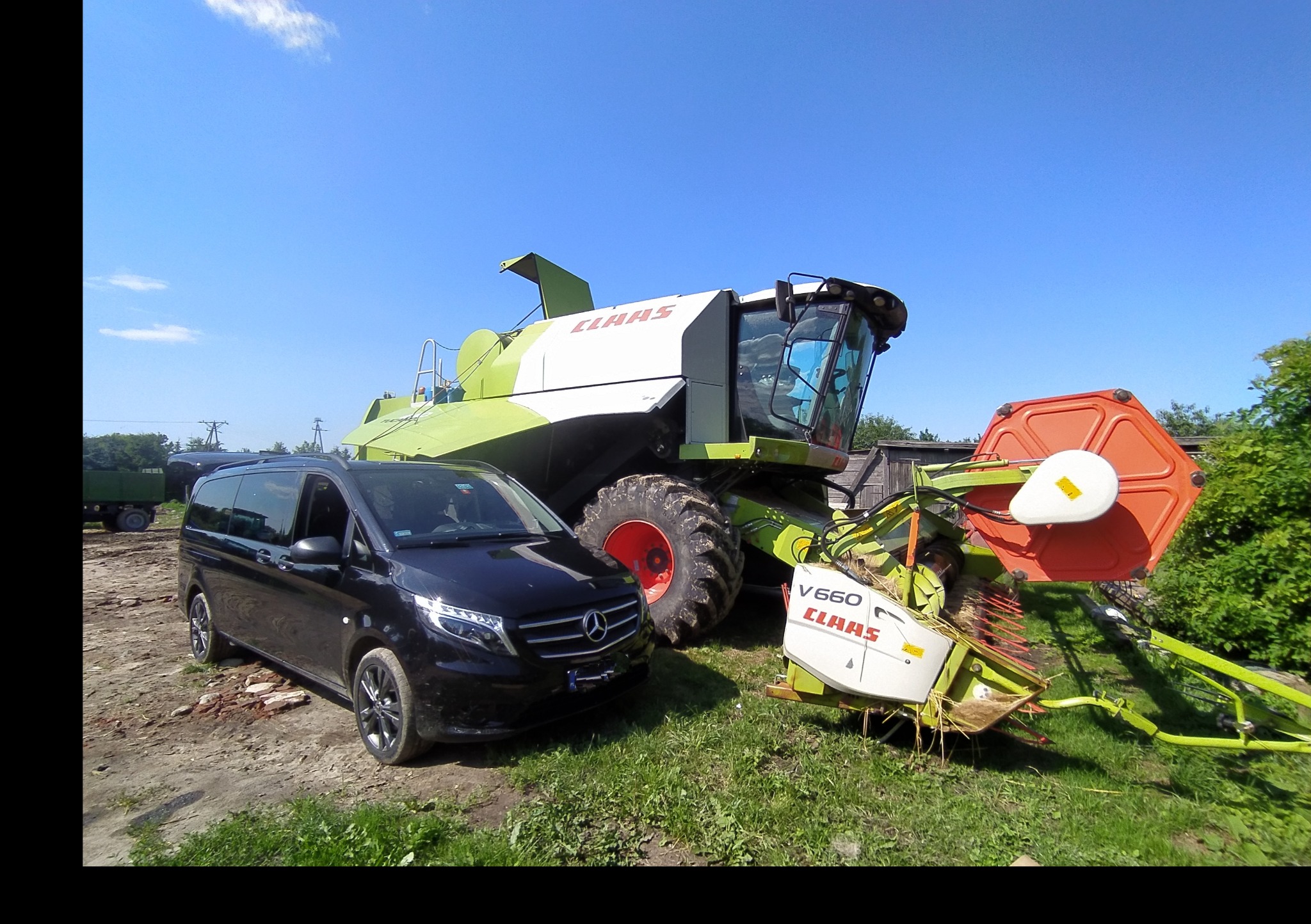 Czarny Mercedes V-klasy zaparkowany obok kombajnu zbożowego marki Claas na polu w słoneczny dzień.