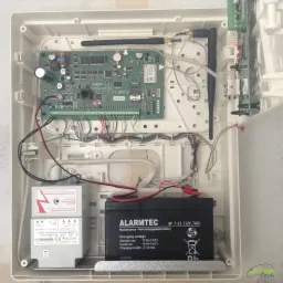 Wnętrze obudowy centrali alarmowej z akumulatorem i transformatorem, instalacja w Bolszewie, widoczne przewody i elektronika.