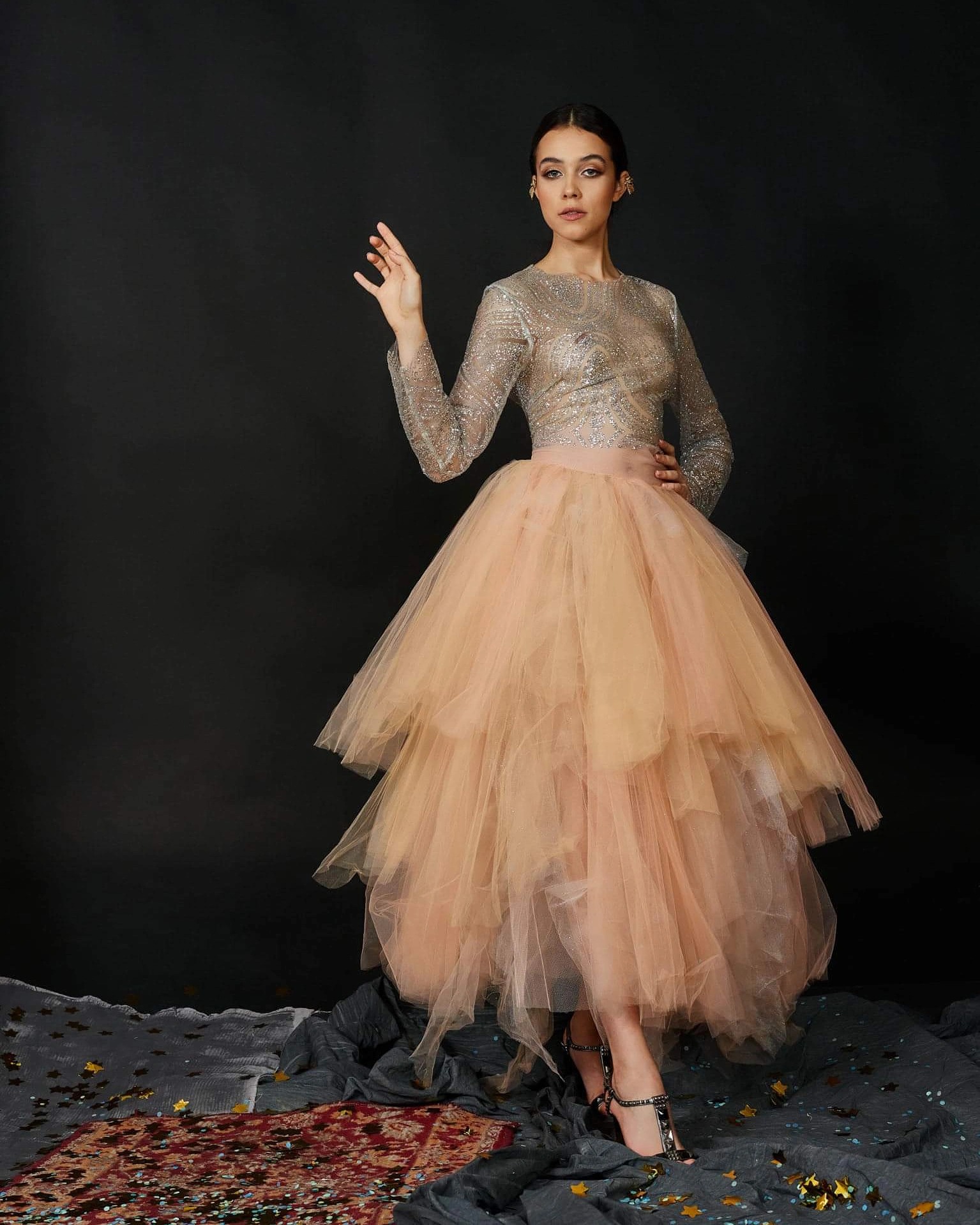 Portret kobiety w srebrzystej bluzce i warstwowej, morelowej spódnicy tiulowej, z delikatnym upięciem włosów i subtelnym, wieczorowym podkreśleniem oczu, pozującej na tle ciemnego tła.