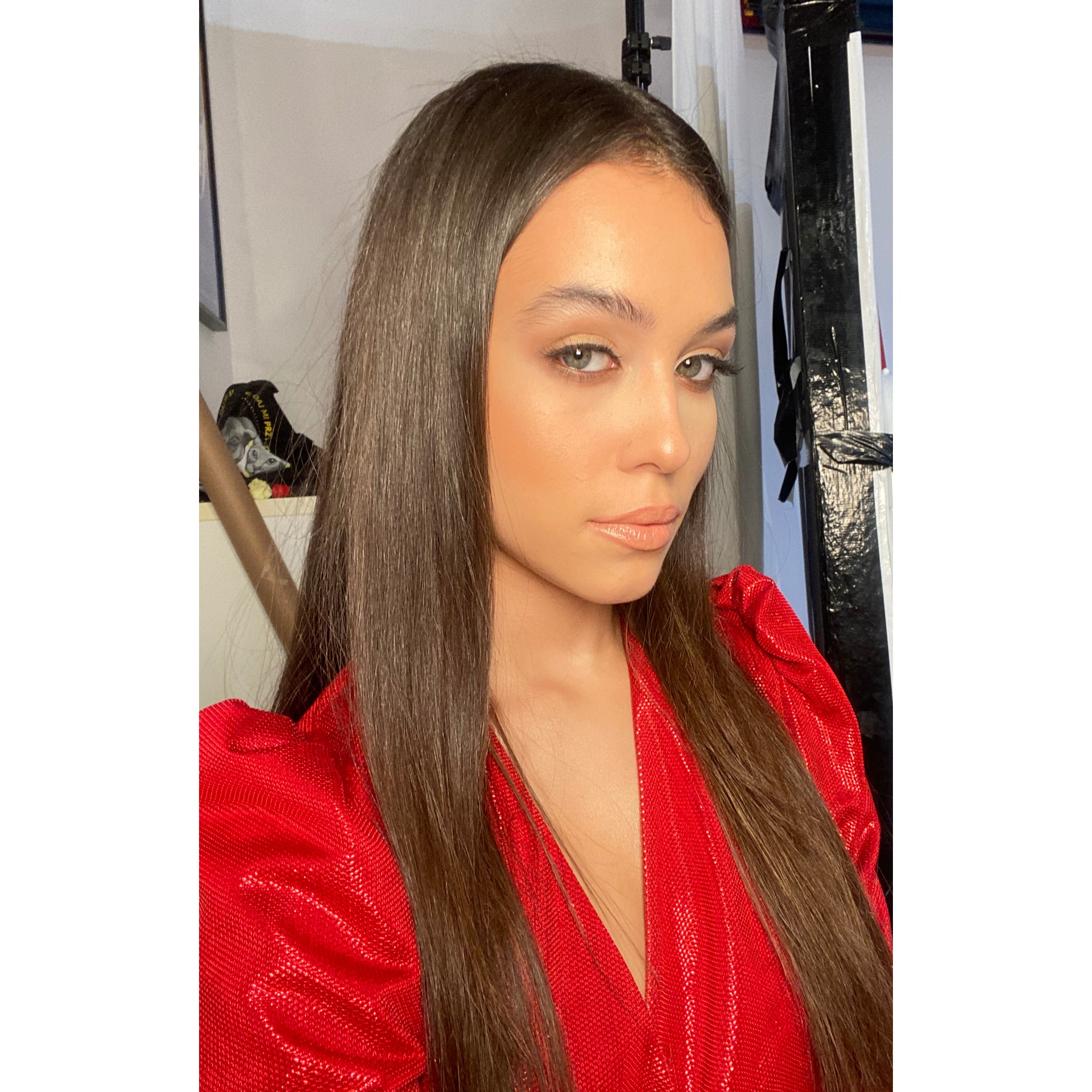 Portret kobiety z subtelnym, błyszczącym wykończeniem, podkreślającym kości policzkowe i usta, na tle studyjnym z elementami oświetlenia.