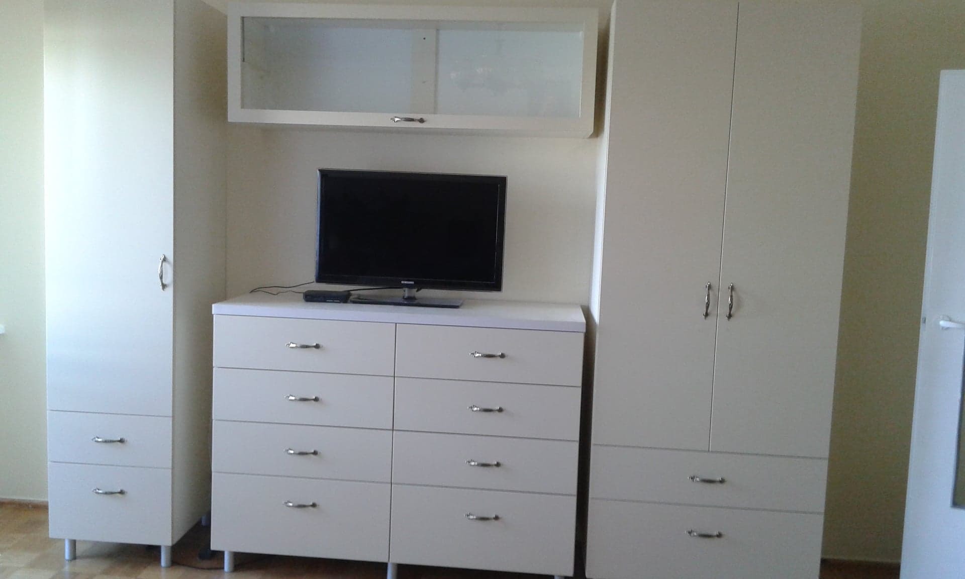 Jasna zabudowa meblowa z szafami i komodą pod telewizor w pokoju.