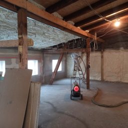 ET Centrum Izolacji - Poddasze ocieplane pianką PUR, widoczny pracownik na drabinie aplikujący pianę, drewniana konstrukcja dachu, nagrzewnica na kółkach, płyty gipsowe w rogu pomieszczenia.