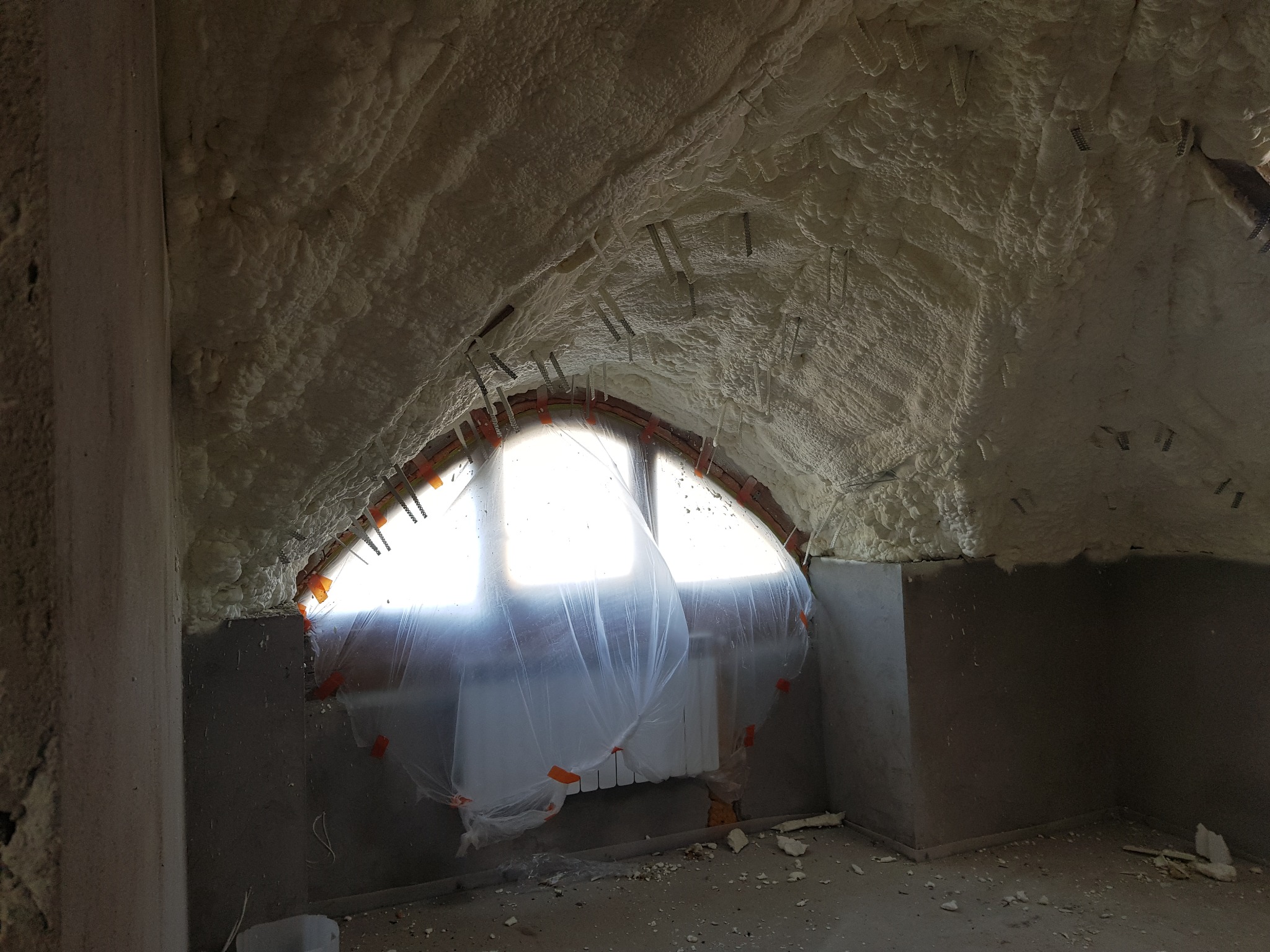 Poddasze po ociepleniu pianką, widoczne wystające elementy montażowe w pianie, okno zabezpieczone folią, surowy stan wykończenia.