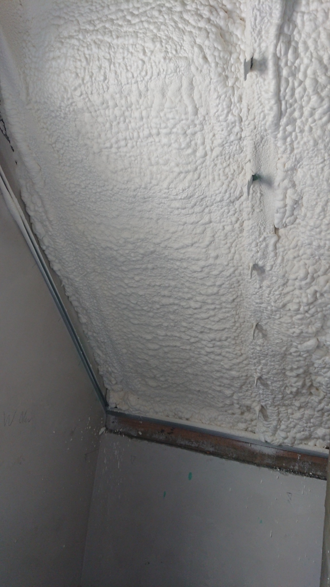 Poddasze ocieplone białą pianką poliuretanową, widoczne elementy konstrukcyjne dachu i ściany, z bliska widoczna struktura pianki.