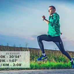 Mężczyzna w zielonej bluzie i czarnych legginsach biegnie w plenerze, dynamiczne ujęcie w locie z widocznymi rekordami biegowymi nałożonymi na obraz.