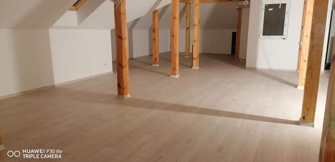 Poddasze z drewnianymi słupami nośnymi i jasną podłogą panelową po zakończeniu prac. Widoczne białe ściany i okno dachowe.