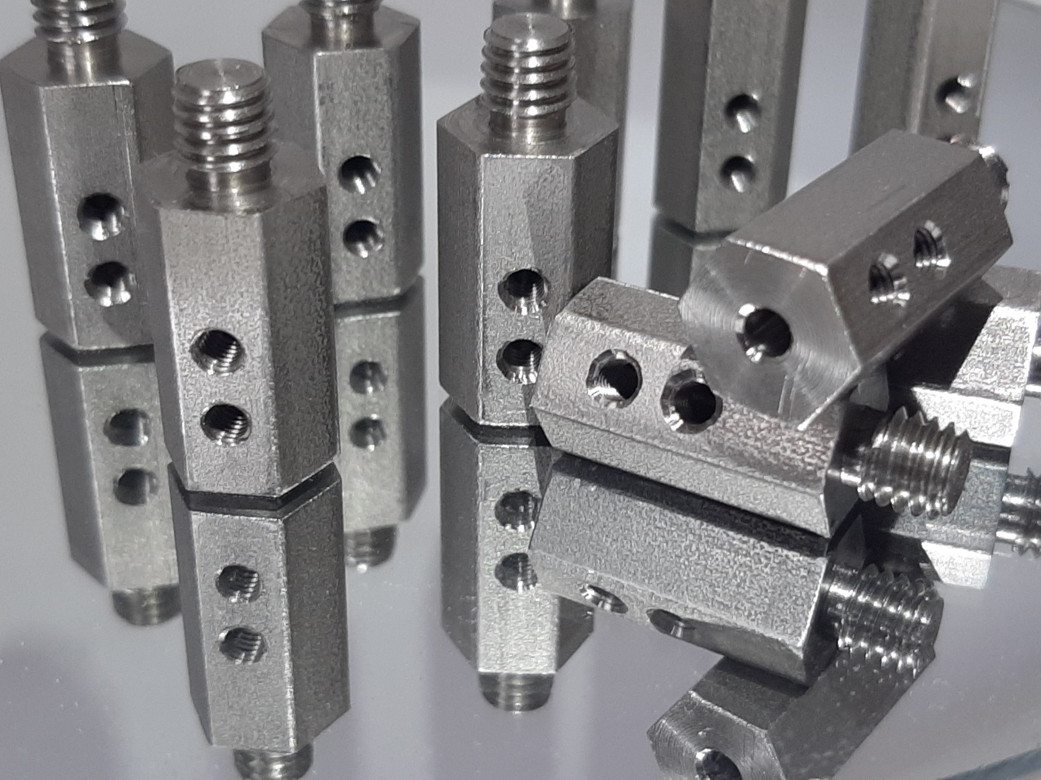 Precyzyjnie wykonane, metalowe elementy z gwintowanymi końcówkami i otworami, ułożone na lustrzanej powierzchni, ukazujące detale obróbki.