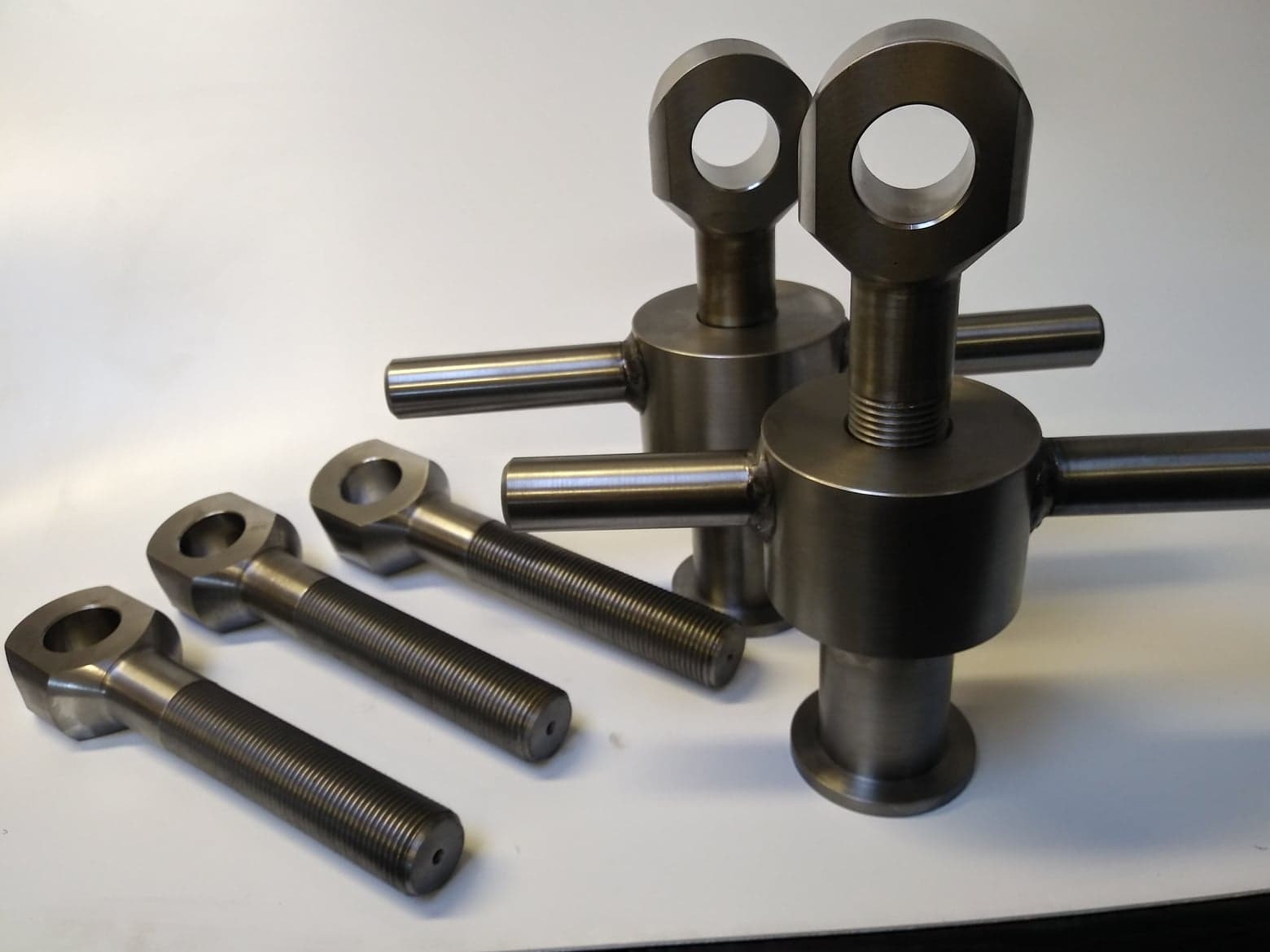 Metalowe elementy z gwintem i otworem, stojące i leżące, wykonane z precyzją, widoczne ślady obróbki.