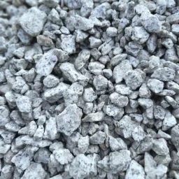 Szary żwir granitowy o nieregularnych kształtach, z widocznymi ciemnymi plamkami, tworzący gęstą teksturę.