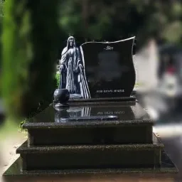 Czarny, dwupoziomowy pomnik z ciemnego granitu z wyrzeźbioną figurą kobiety w szatach i wazonem, umieszczony na tle zieleni cmentarza.