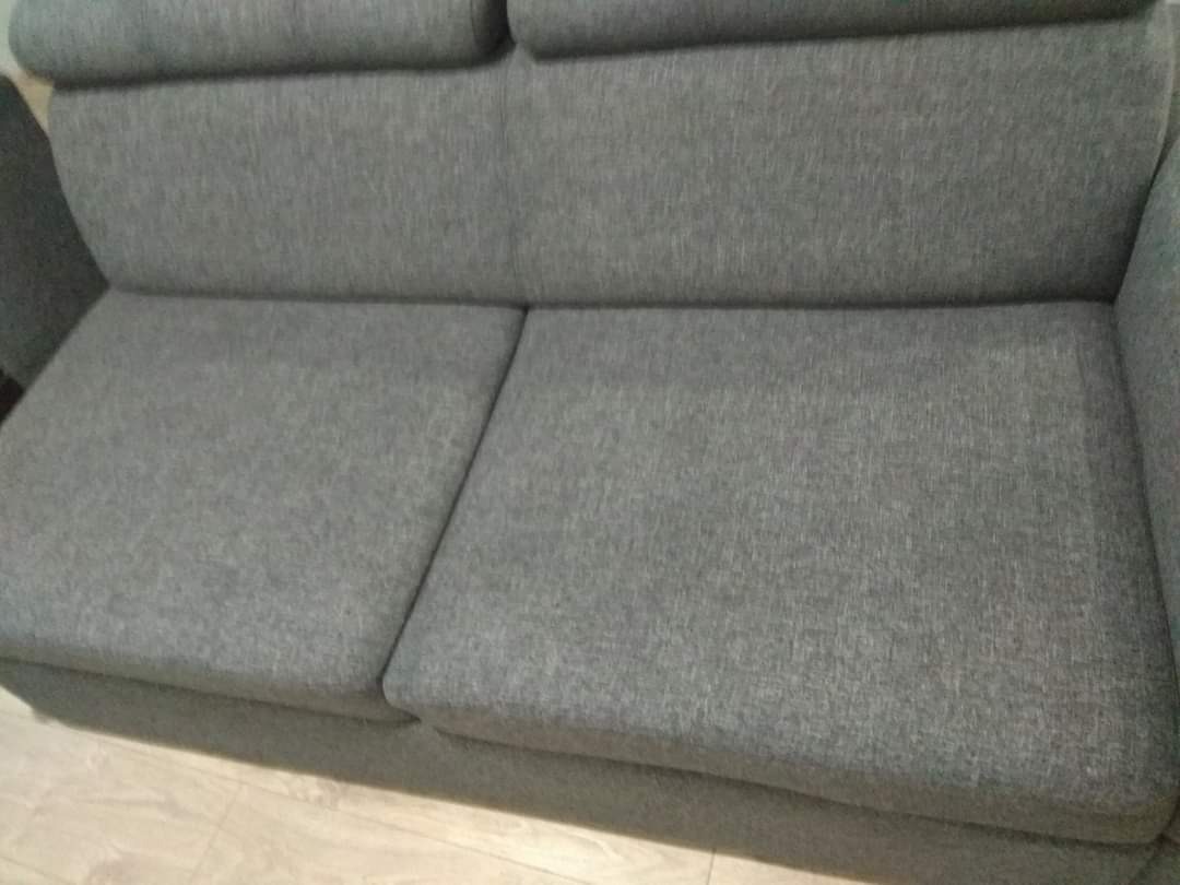 Szara, dwuosobowa kanapa z tapicerką o wyraźnej fakturze, widziana z bliska, z delikatnym oświetleniem podkreślającym detale tkaniny.