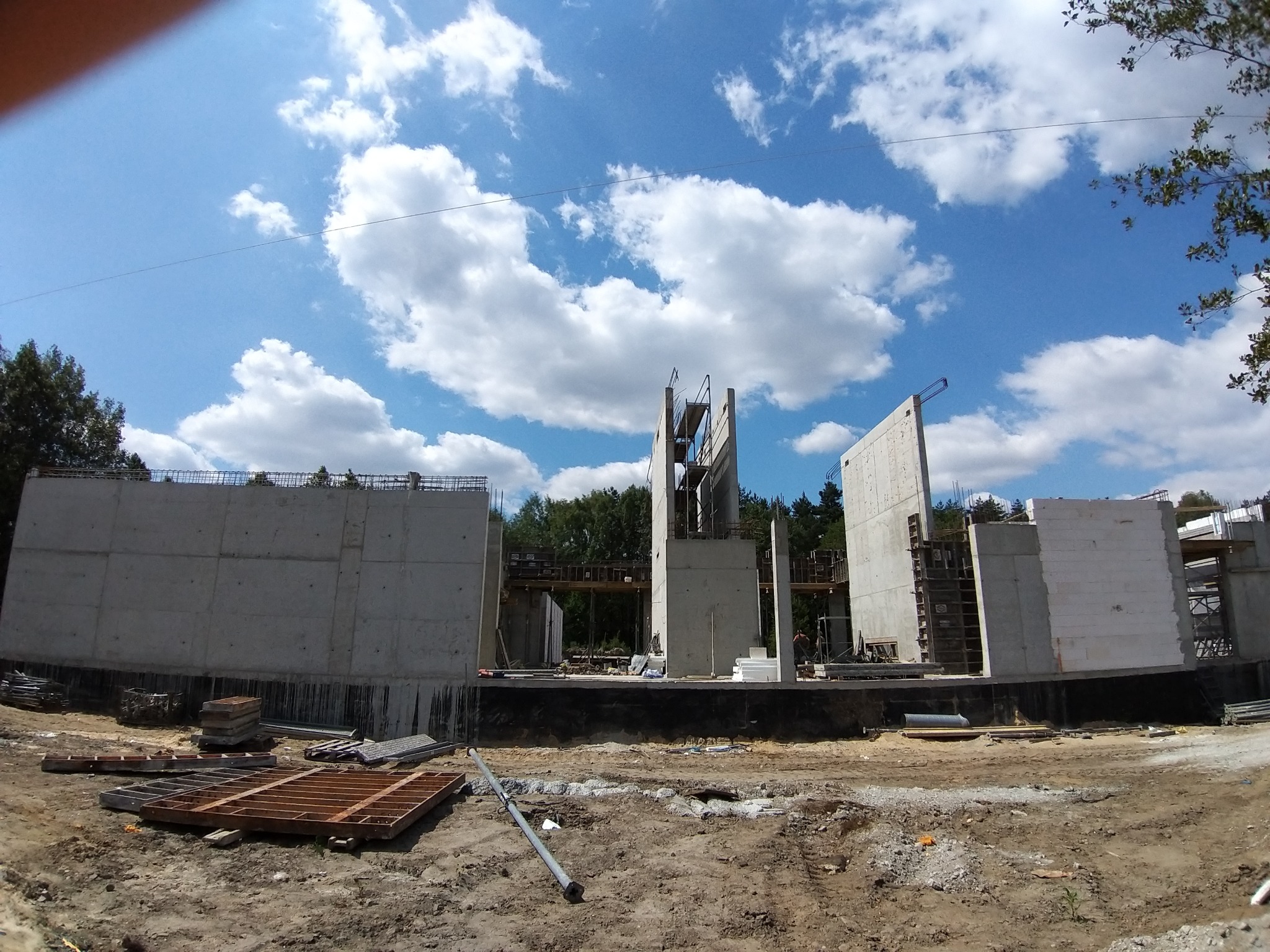Wznoszenie konstrukcji żelbetowej budynku w słoneczny dzień, widoczne szalunki i zbrojenia, w tle las.
