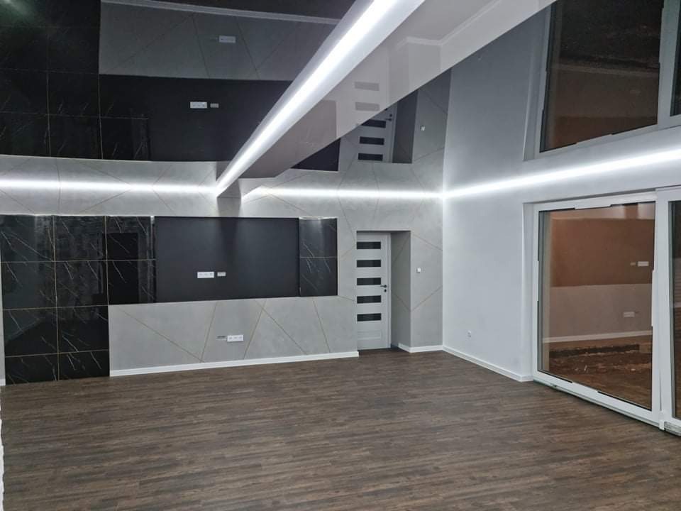 Nowoczesne wnętrze: ciemna, lakierowana podłoga, ściany w odcieniach szarości z dekoracyjnymi panelami i oświetleniem LED, drzwi wewnętrzne z poziomymi przeszkleniami, duże okno przesuwne.