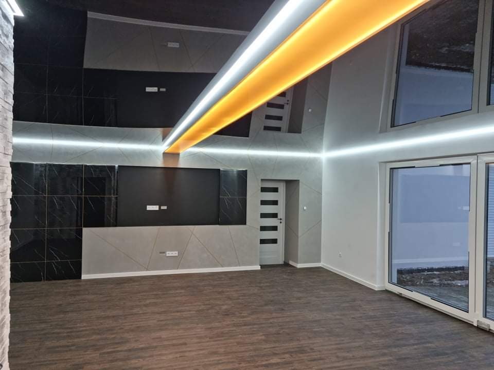 Nowoczesne wnętrze z panelami ściennymi imitującymi marmur, podświetlanym sufitem i panelami podłogowymi w odcieniach brązu, widoczne gładkie ściany i duże okno przesuwne.