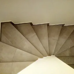 Spiralne schody wyłożone szarymi płytkami, widok z góry, z widocznymi detalami fug i krawędzi schodów.