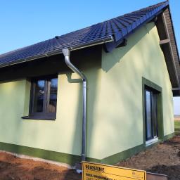 www.domyzkeramzytu.pl-Krotoszyn - Nowo wybudowany, parterowy dom z jasnozieloną elewacją, ciemną dachówką i metalową rynną, na działce z częściowo wyrównanym terenem.