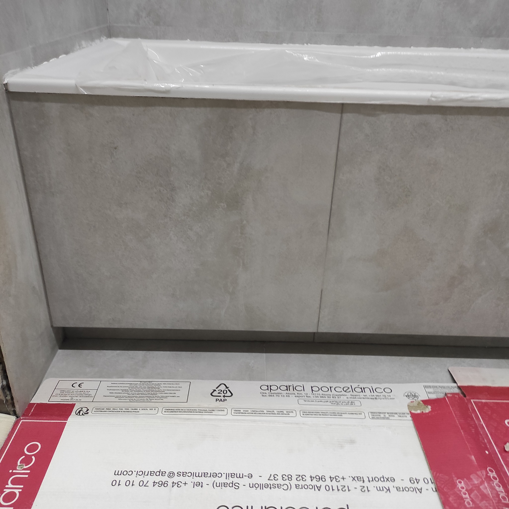 Obudowa wanny wykończona płytkami w odcieniach szarości. Widoczne opakowania po płytkach Aparici. Całość sprawia wrażenie świeżo wykończonej.