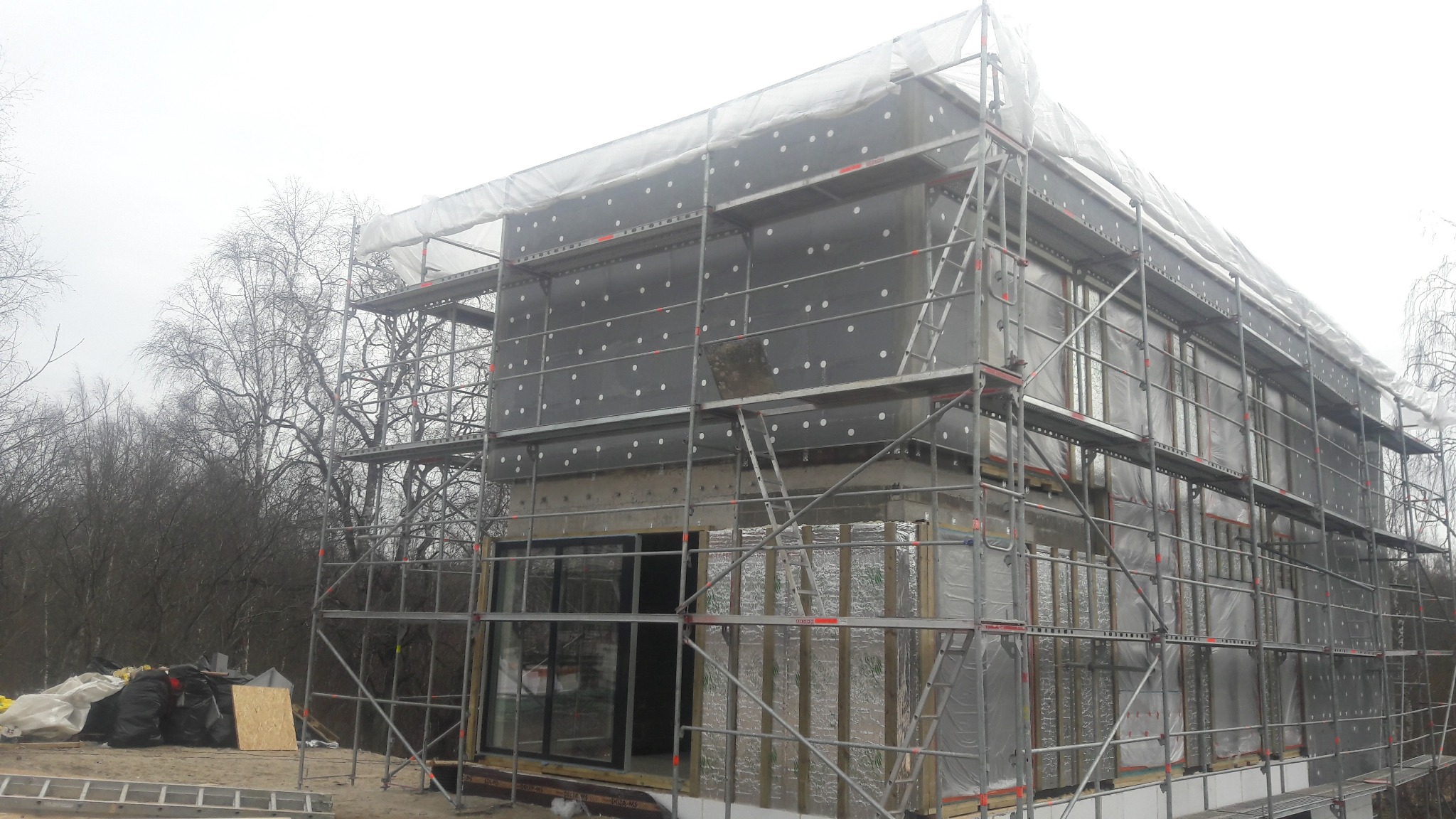 Ocieplanie domu w Mińsku Mazowieckim. Budynek w trakcie izolacji, widoczne rusztowania i materiały izolacyjne. Etap prac przed wykończeniem elewacji.