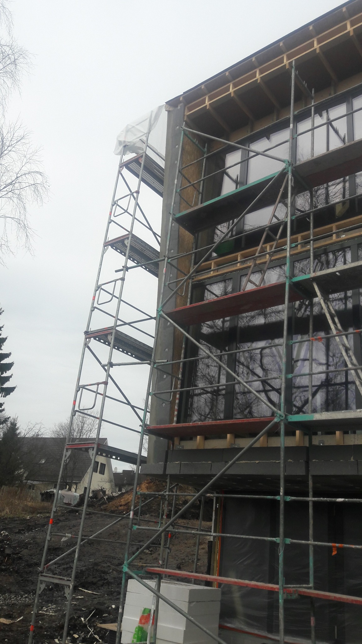 Budynek w trakcie ocieplania, widoczne rusztowania, styropian i okna. Prace na wysokościach w pochmurny dzień. Elementy konstrukcyjne i materiały izolacyjne.