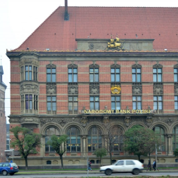 Przedsiębiorstwo Budowlane TB.INVEST Tomasz Brzeziński - Fasada budynku Narodowego Banku Polskiego z czerwonej cegły, zdobiona ornamentami i rzeźbami, z widocznym napisem 'NARODOWY BANK POLSKI' oraz złotą statuetką żaglowca na szczycie, na tle szarego...