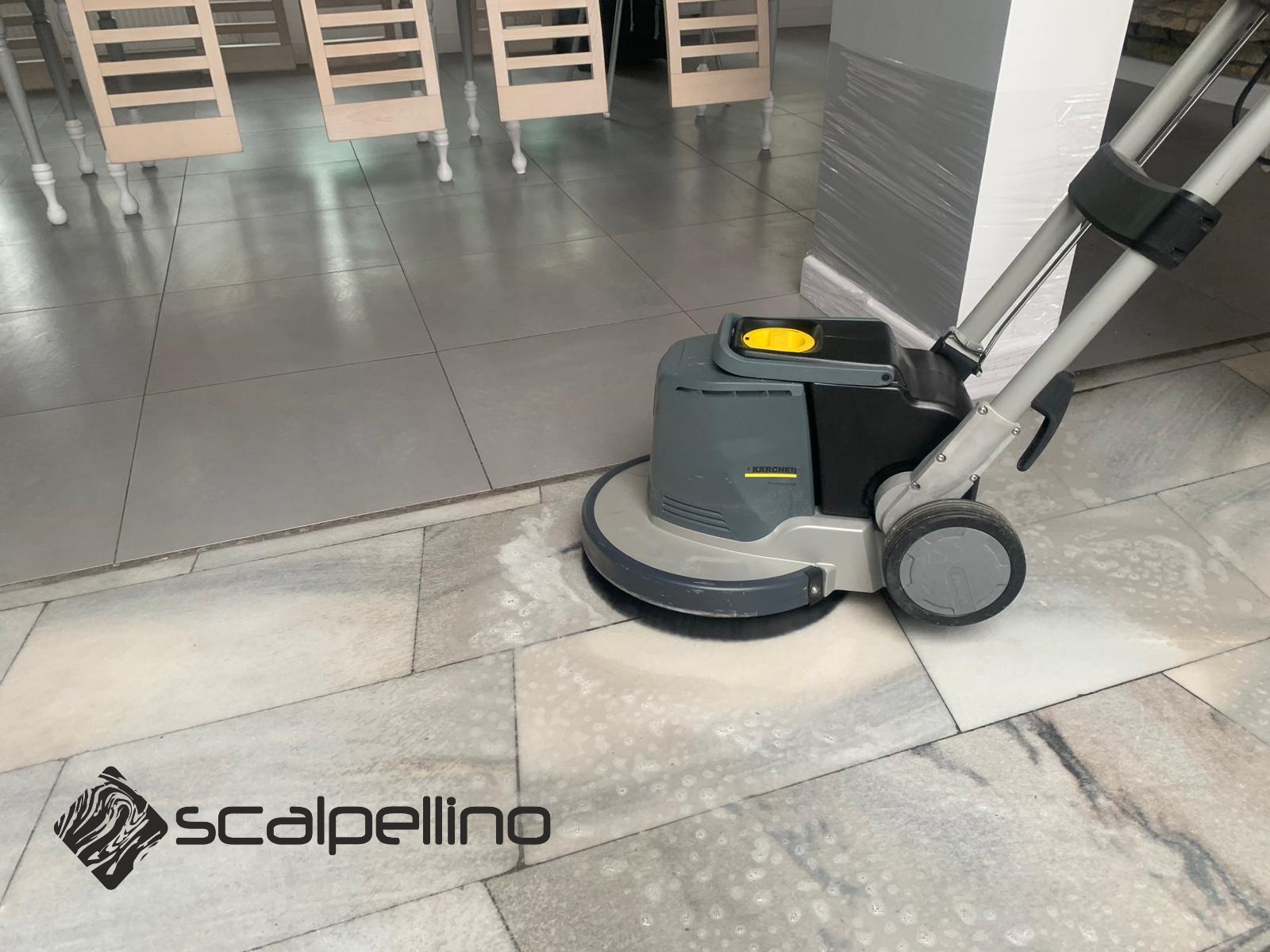 Szorowarka Karcher w trakcie czyszczenia marmurowej podłogi w pomieszczeniu, widoczne ślady mokrej powierzchni, w tle krzesła i kolumna zabezpieczona folią.