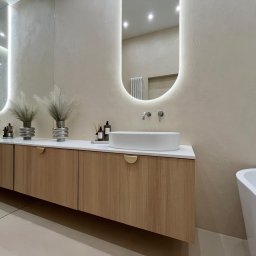 Pracownia Projektowa Dorota Wróbel - Nowoczesna łazienka z drewnianą szafką pod umywalką, owalnym lustrem z podświetleniem LED i dekoracyjnymi wazonami z trawą pampasową. Minimalistyczny design, ciepła kolorystyka.