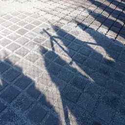 Ułożona kostka brukowa z wypełnionymi szczelinami drobnym kruszywem, oświetlona słońcem z widocznymi cieniami