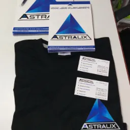 Materiały reklamowe firmy Astralix: notatniki, wizytówki i czarny t-shirt z logo, prezentujące usługi wycinania laserowego, spawania laserowego, pras krawędziowych, tokarek CNC i frezarek CNC.