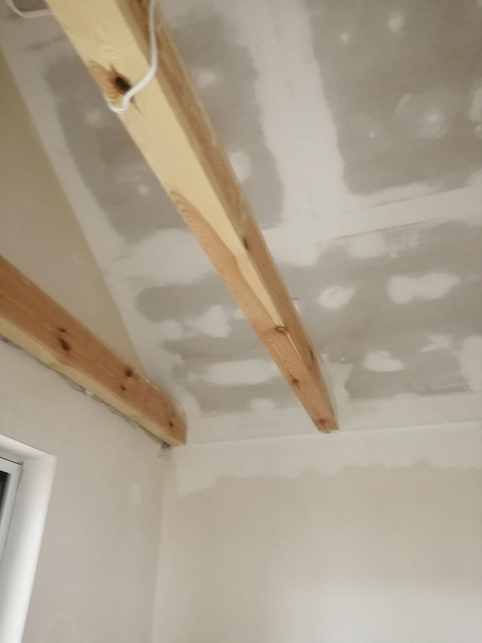 Skośny sufit z widocznymi drewnianymi belkami i wstępnie nałożoną warstwą szpachli, widok z dołu na niedokończone wnętrze.