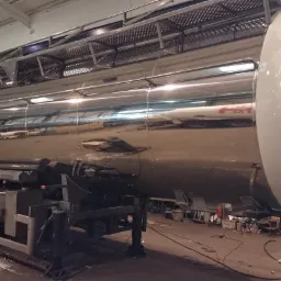 Błyszcząca, chromowana cysterna samochodowa z elementami ze stali nierdzewnej, widoczna w hali warsztatowej podczas prac konserwacyjnych.