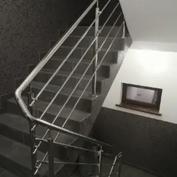 Wewnętrzne schody z szarymi stopniami i nowoczesną balustradą ze stali nierdzewnej z poziomymi wypełnieniami, widok z dołu, małe okno w ścianie na półpiętrze.