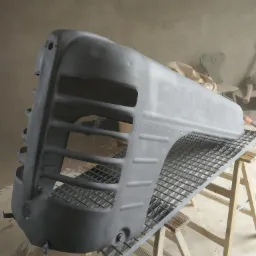 Szary, odnowiony grill traktora na metalowej kratce, wspartej na drewnianych kozłach, w warsztacie.