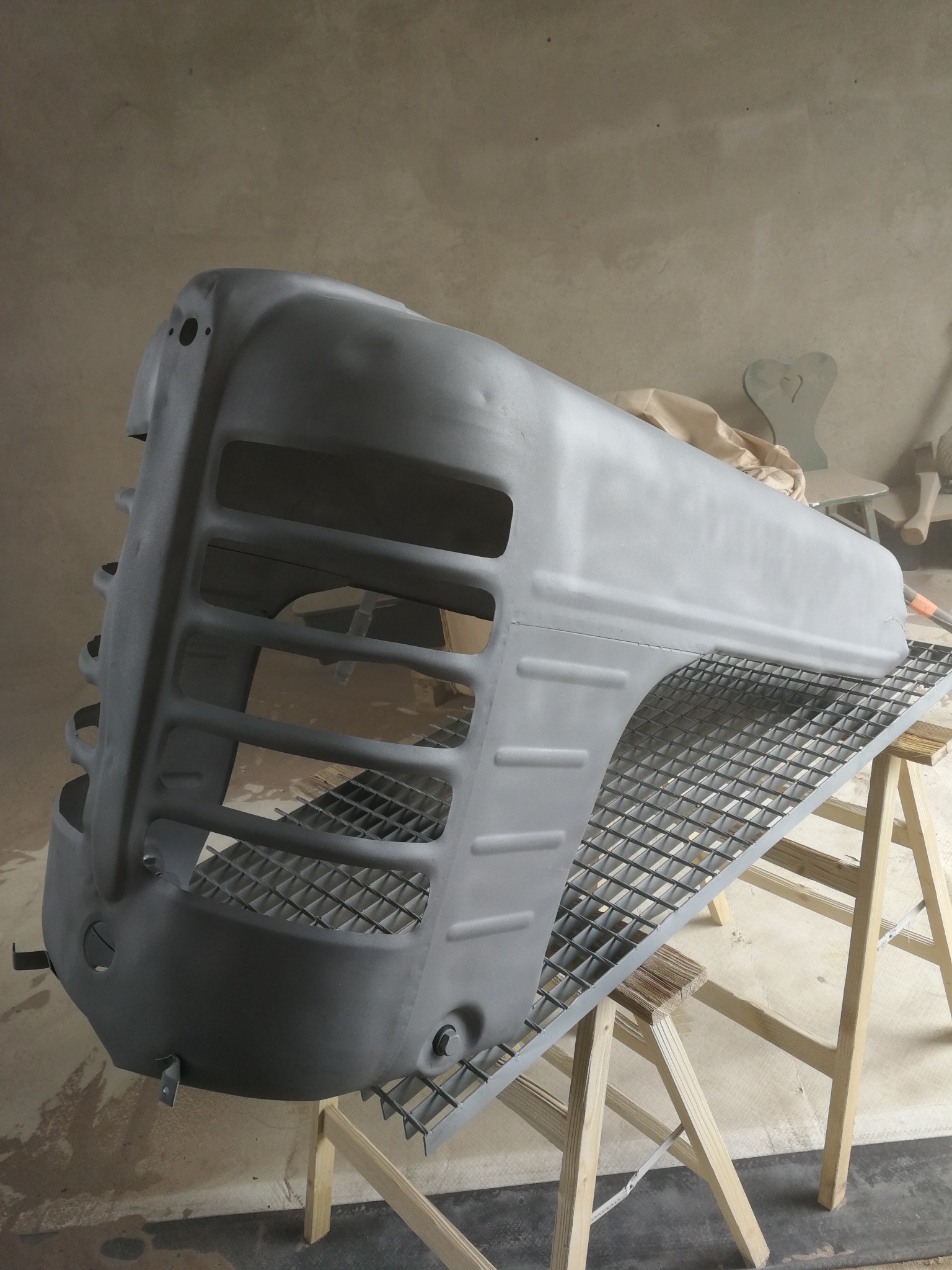 Szary, odnowiony grill traktora na metalowej kratce, wspartej na drewnianych kozłach, w warsztacie.