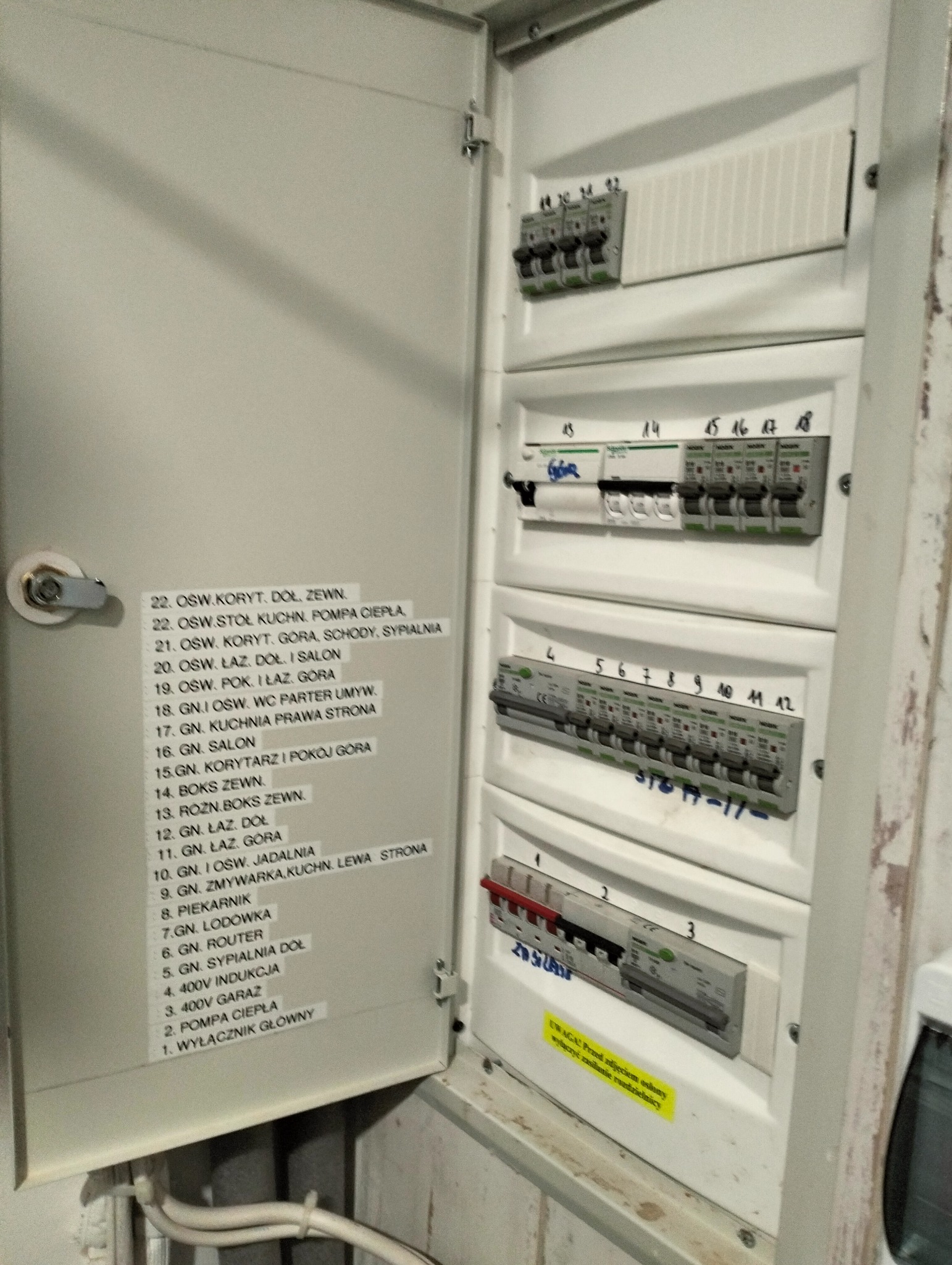 Otwarta skrzynka elektryczna z widocznymi bezpiecznikami i naklejkami identyfikującymi obwody, z bliska, widoczna instalacja przewodów.